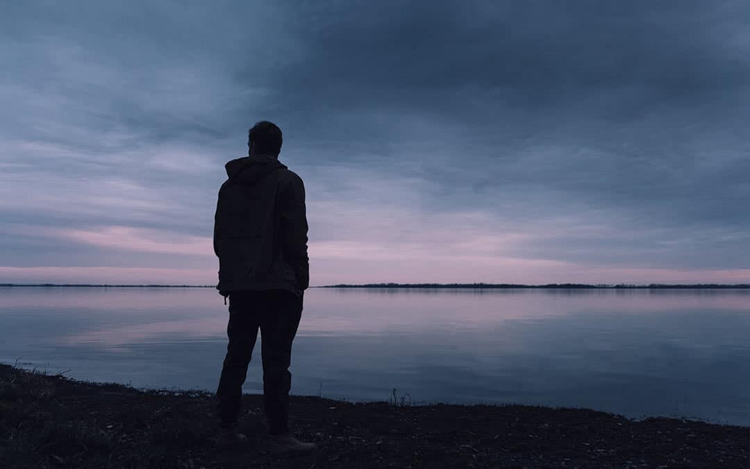 Man standing outside alone on the shore of a lake